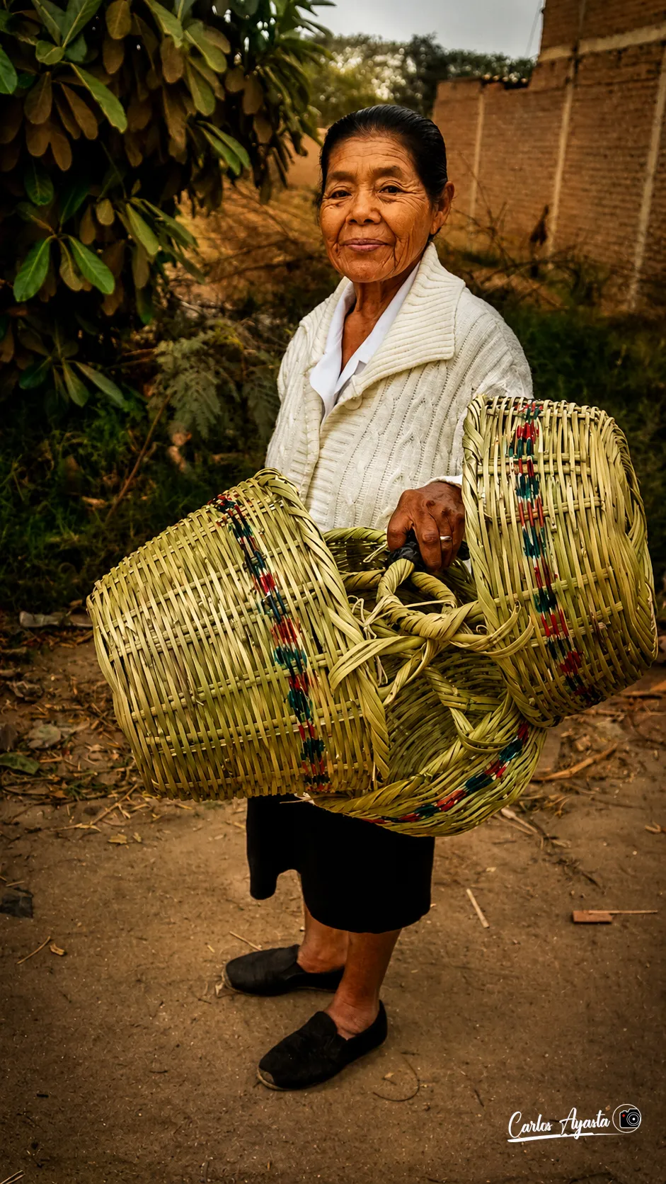 Mujer de pie sosteniendo dos canastas tejidas con fibras vegetales